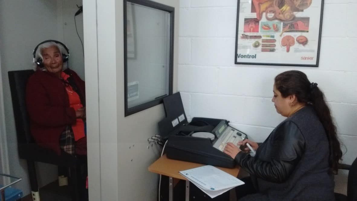 Especialista realizando una audiometría a una paciente adulta mayor en cabina