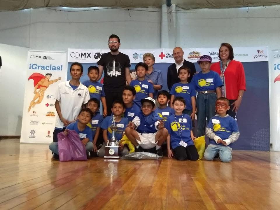 Grupo de niños y voluntarios de Audio Amigo posando con un trofeo durante un evento